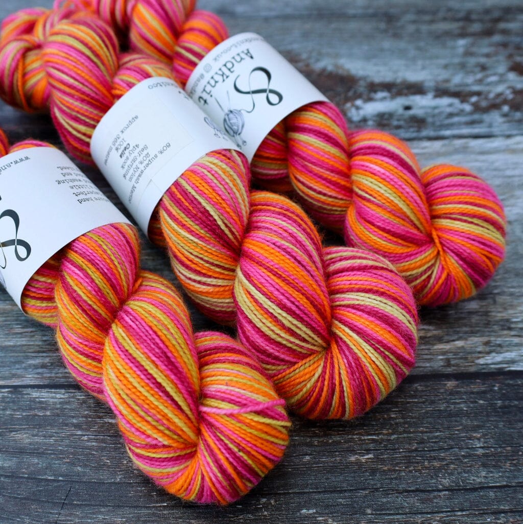 Three skeins of variegated yarn with white paper labels, featuring stripes of orange, pink, and yellow, arranged on a rustic dark wood surface.