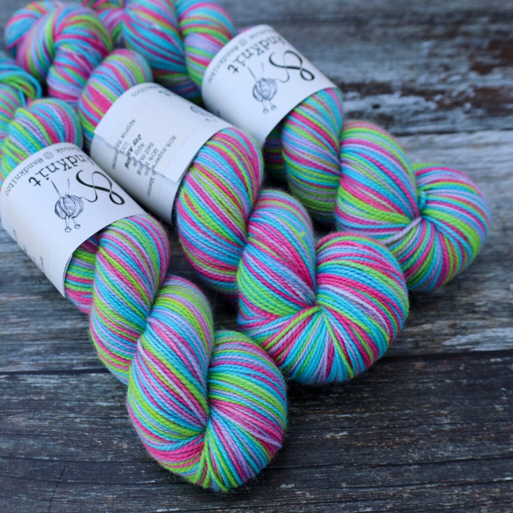 Several skeins of variegated yarn with white paper labels, featuring stripes of pink, blue, green, and purple, arranged on a rustic dark wooden surface.
