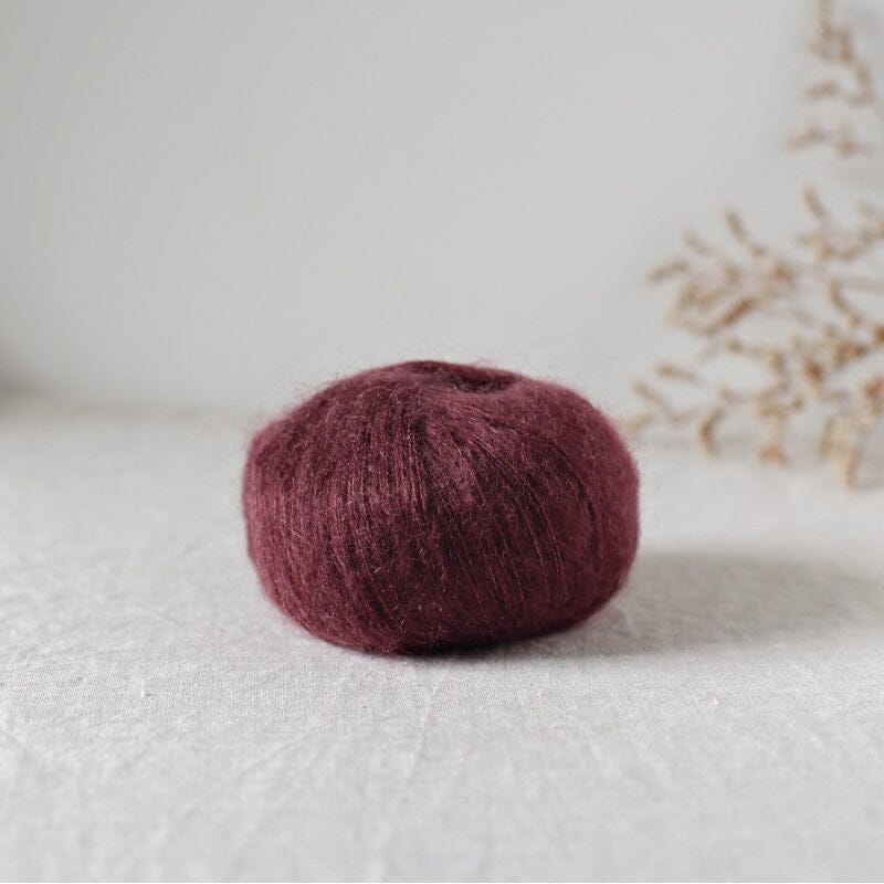 Ball of dark purple yarn on a light surface with a blurred natural background