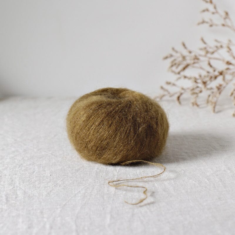 Ball of brown mohair on a white surface with dried branches in the background