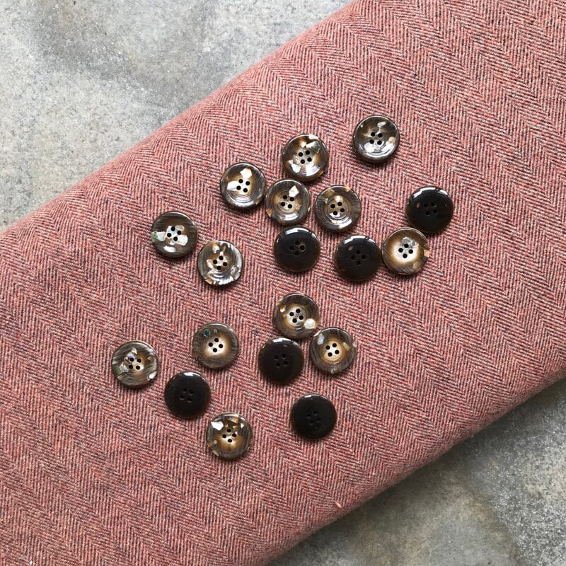 Brown buttons on a textured pink fabric with a hand holding one button.
