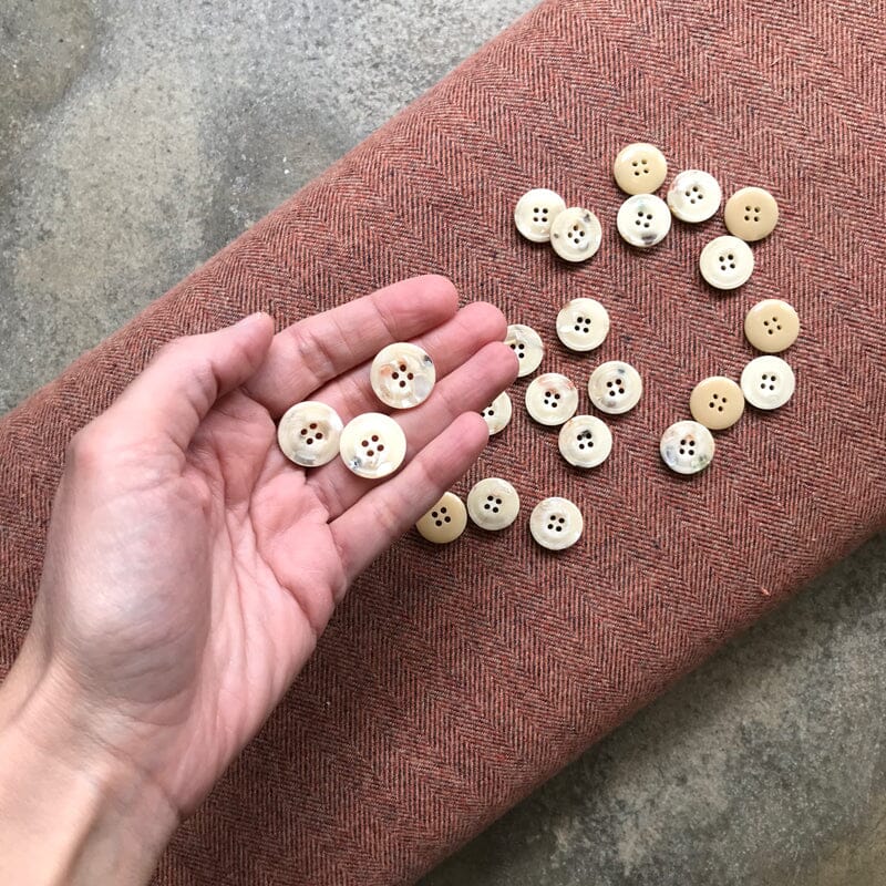 Hand holding buttons with a collection of buttons on a brown fabric surface