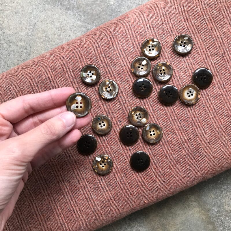 Brown buttons on a textured pink fabric with a hand holding one button.