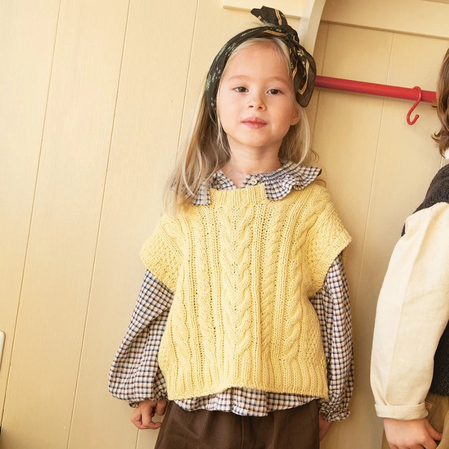 Child wearing a yellow knitted vest over a checkered shirt with a neutral background