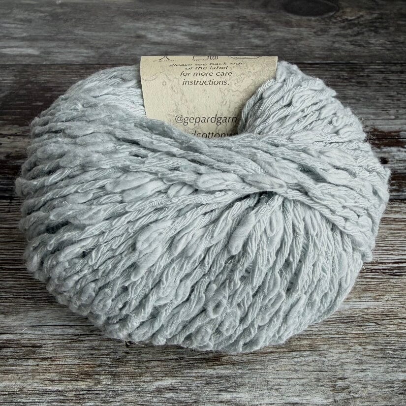 Ball of ice blue cotton boucle yarn on a wooden surface with a label.