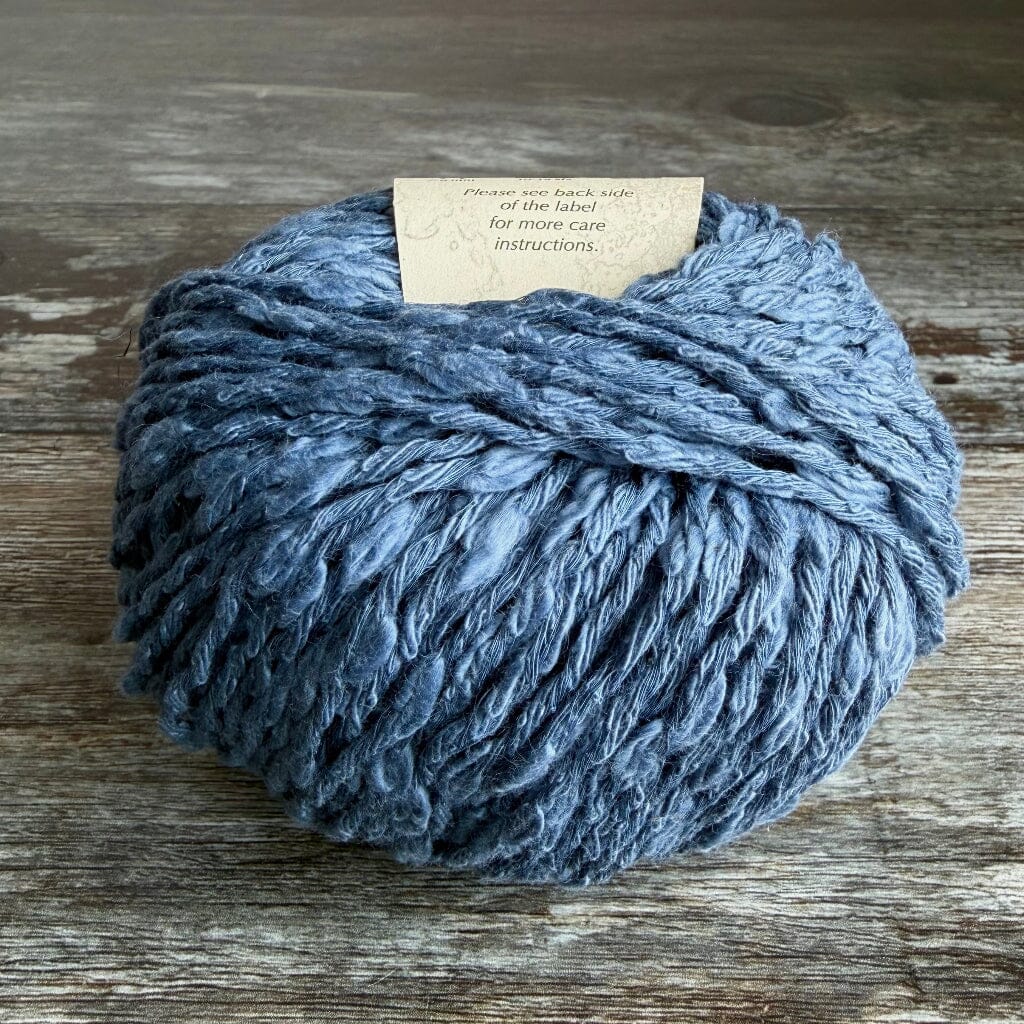 Blue cotton boucle of yarn on a wooden surface with a label attached.