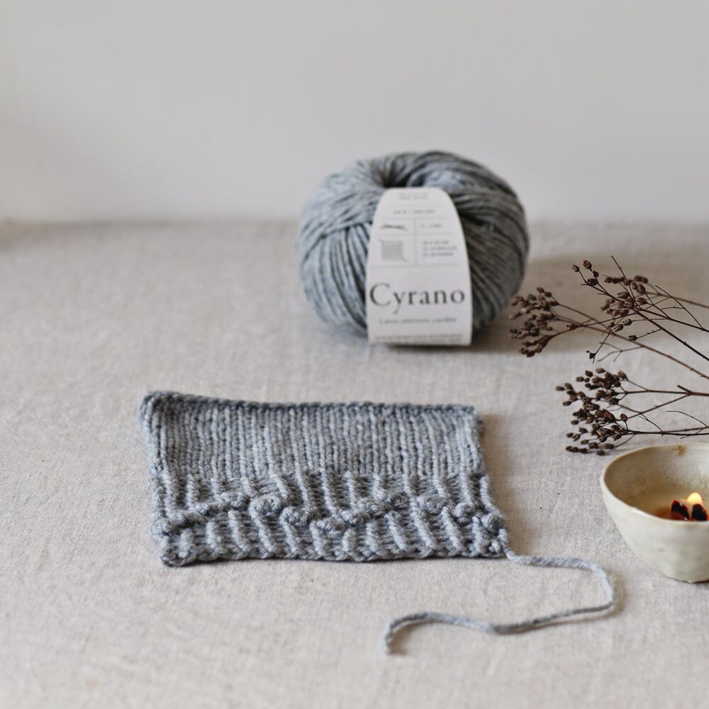 Ball of yarn with a label and knitted fabric on a neutral background
