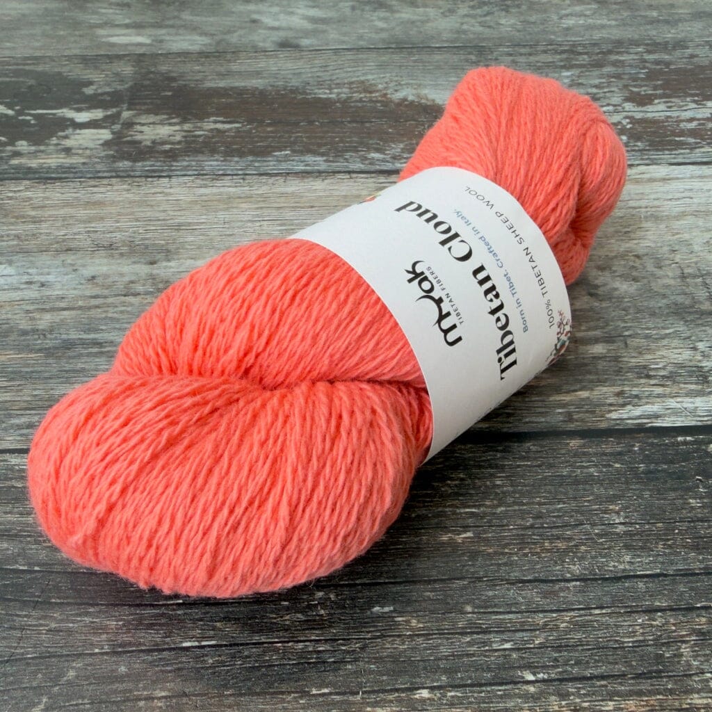 Coral skein of yarn with a label on a wooden surface