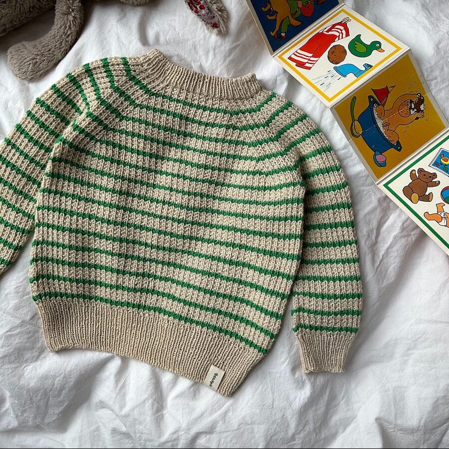 Striped sweater with green and beige pattern on a white surface with toys and books.