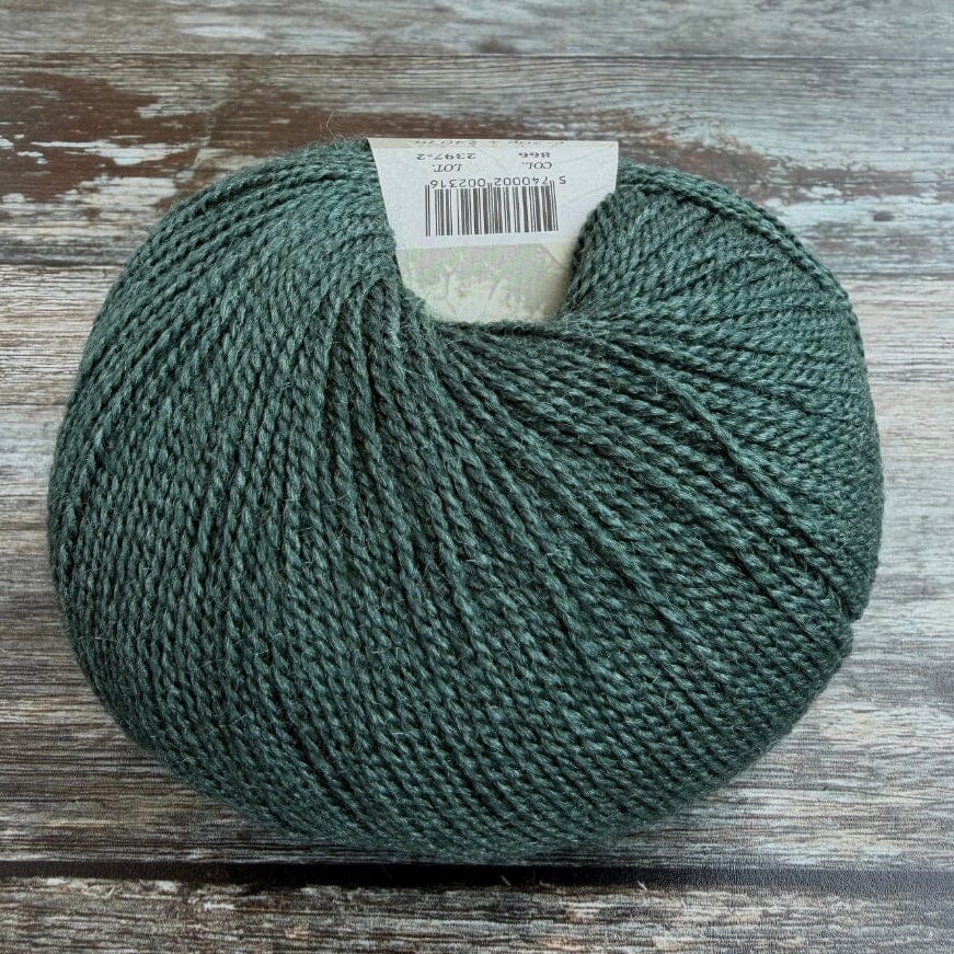 A ball of dark teal-green yarn resting on a rustic, weathered gray-brown wooden surface, with a white paper label visible at the top.