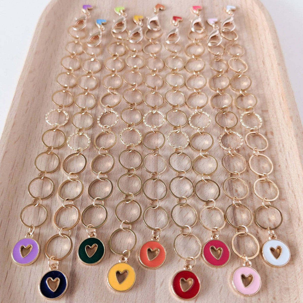 Gold row counter chains with colourful heart charms on a wooden surface