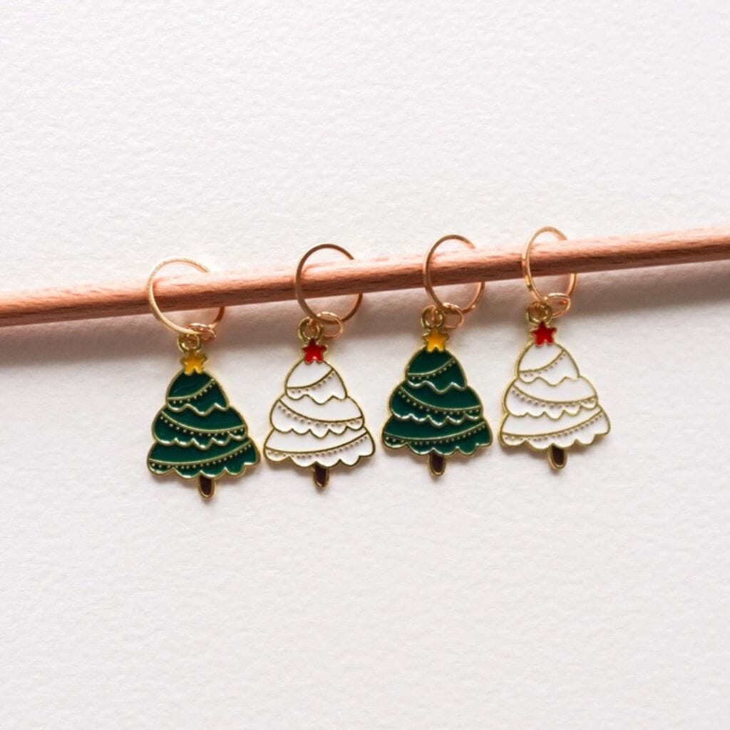Four Christmas tree-shaped knitting stitch markers on a knitting needle against a white background.