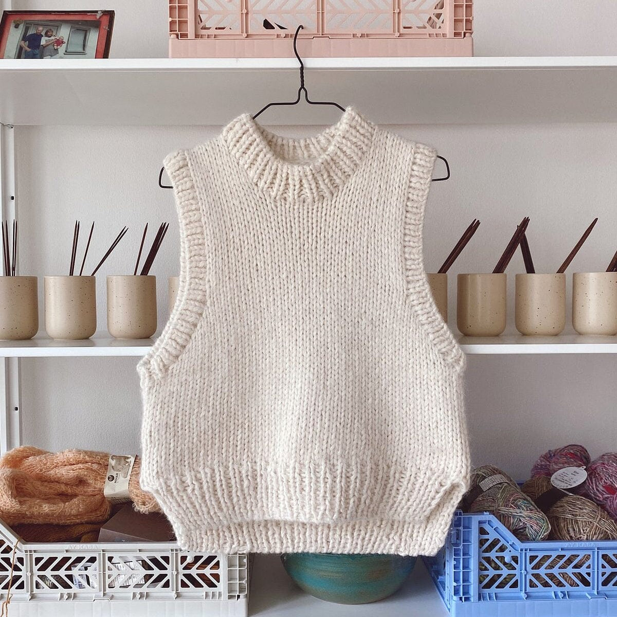 Knitted vest hanging on a hook against a shelf with various items