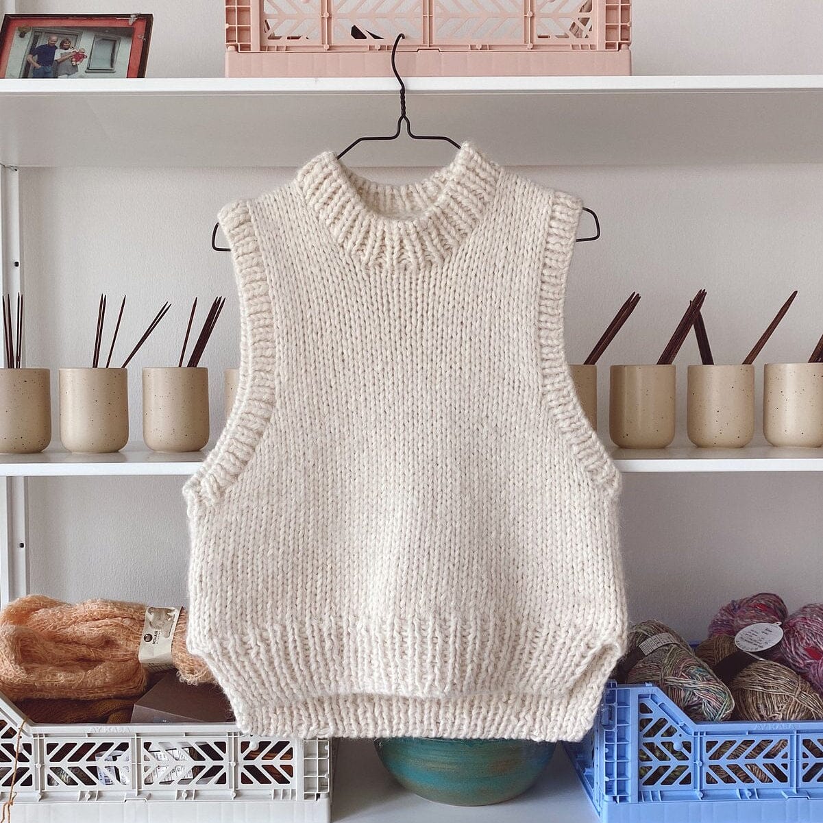 Knitted vest hanging on a hook against a shelf with various items
