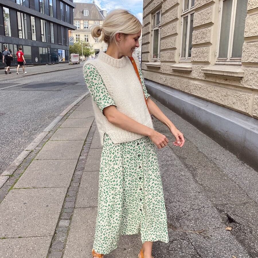 Woman in a green floral dress and beige sweater walking on a street.