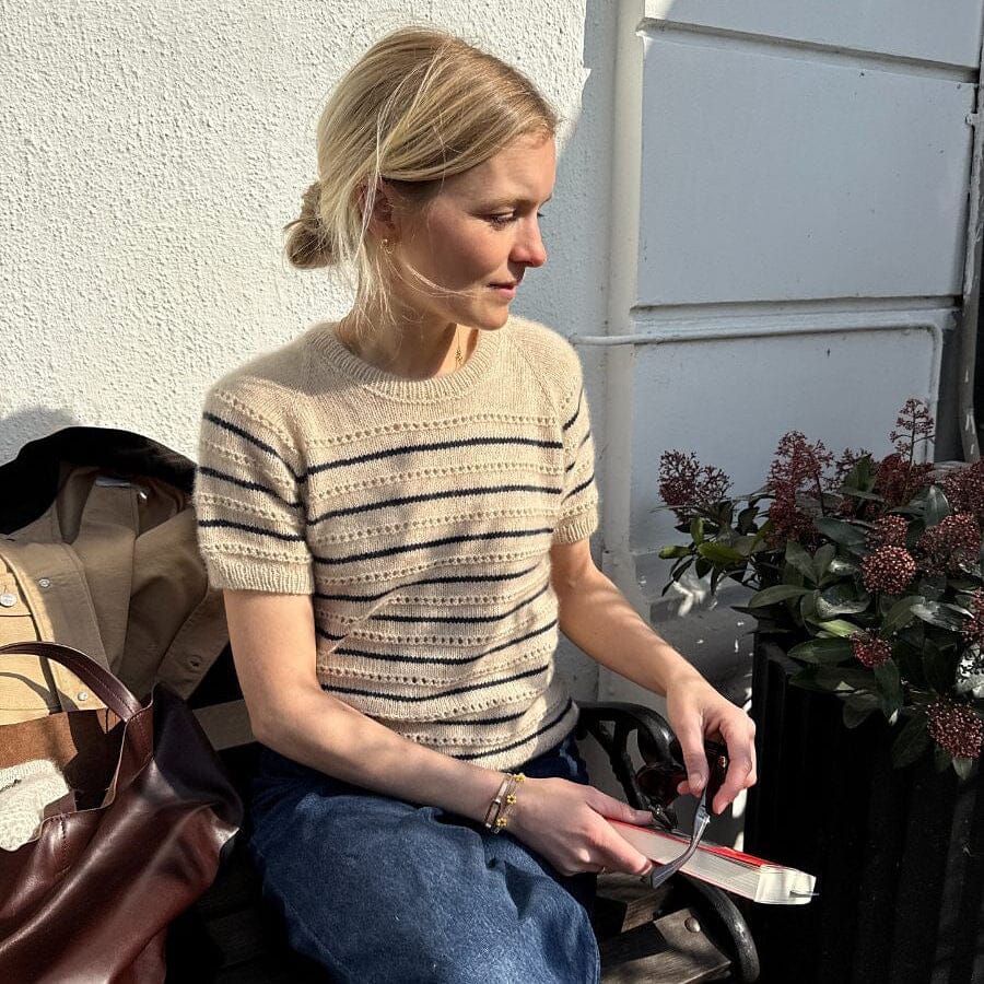 Woman sitting outdoors reading a book with a plant and handbag nearby.