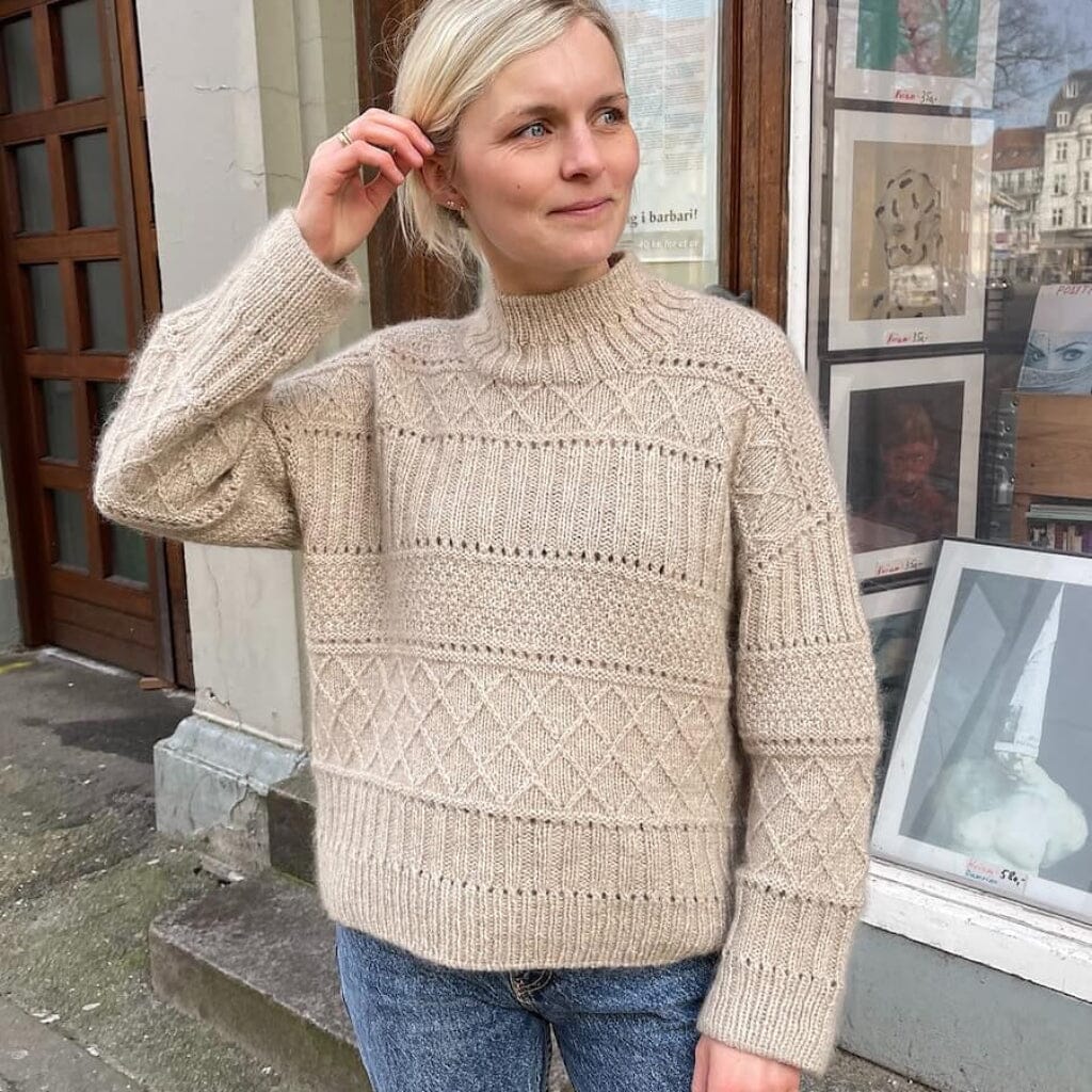 Woman wearing a beige knitted sweater standing in front of a store window.