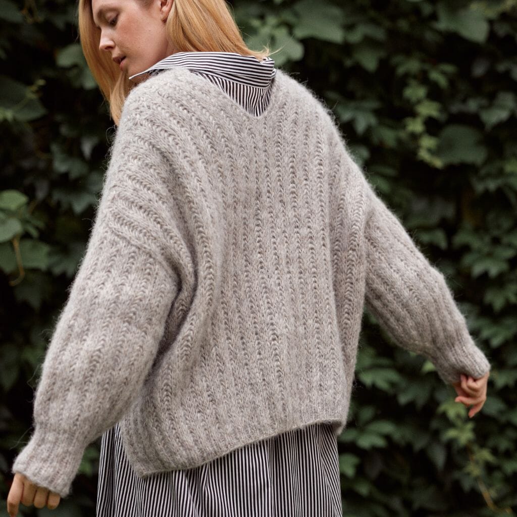 Person wearing a chunky knit sweater with a blurred green foliage background