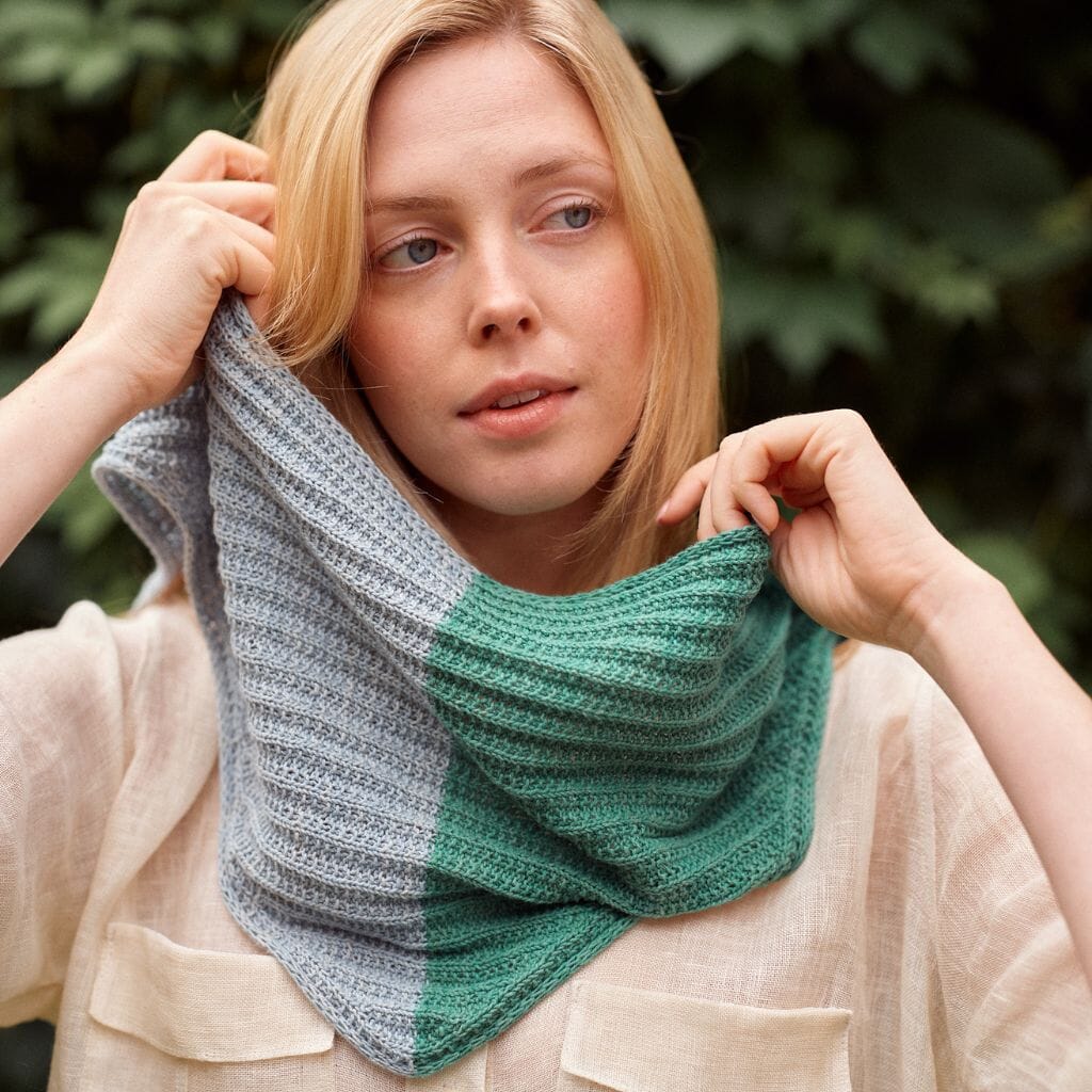 Woman wearing a green and gray knitted scarf against a blurred natural background