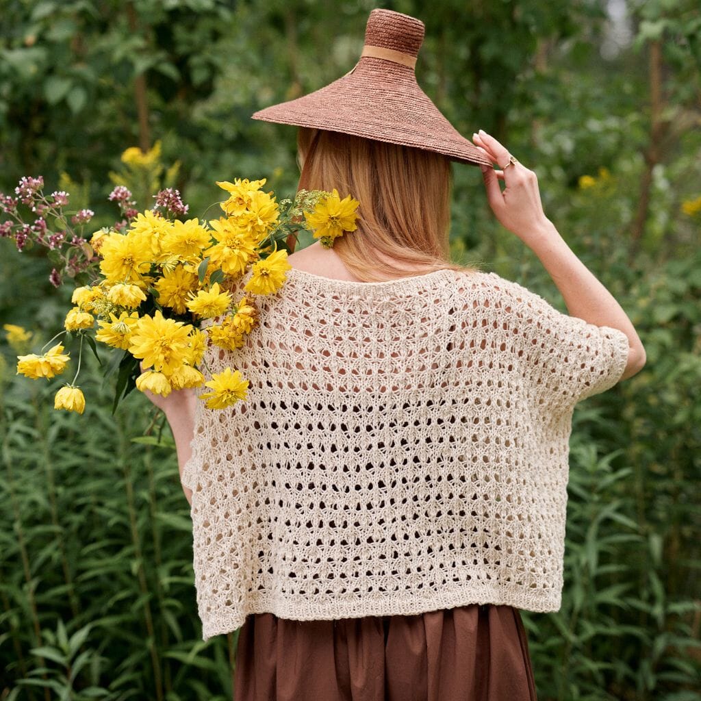 Woman holding a bouquet of yellow flowers and a woven hat in a natural setting.