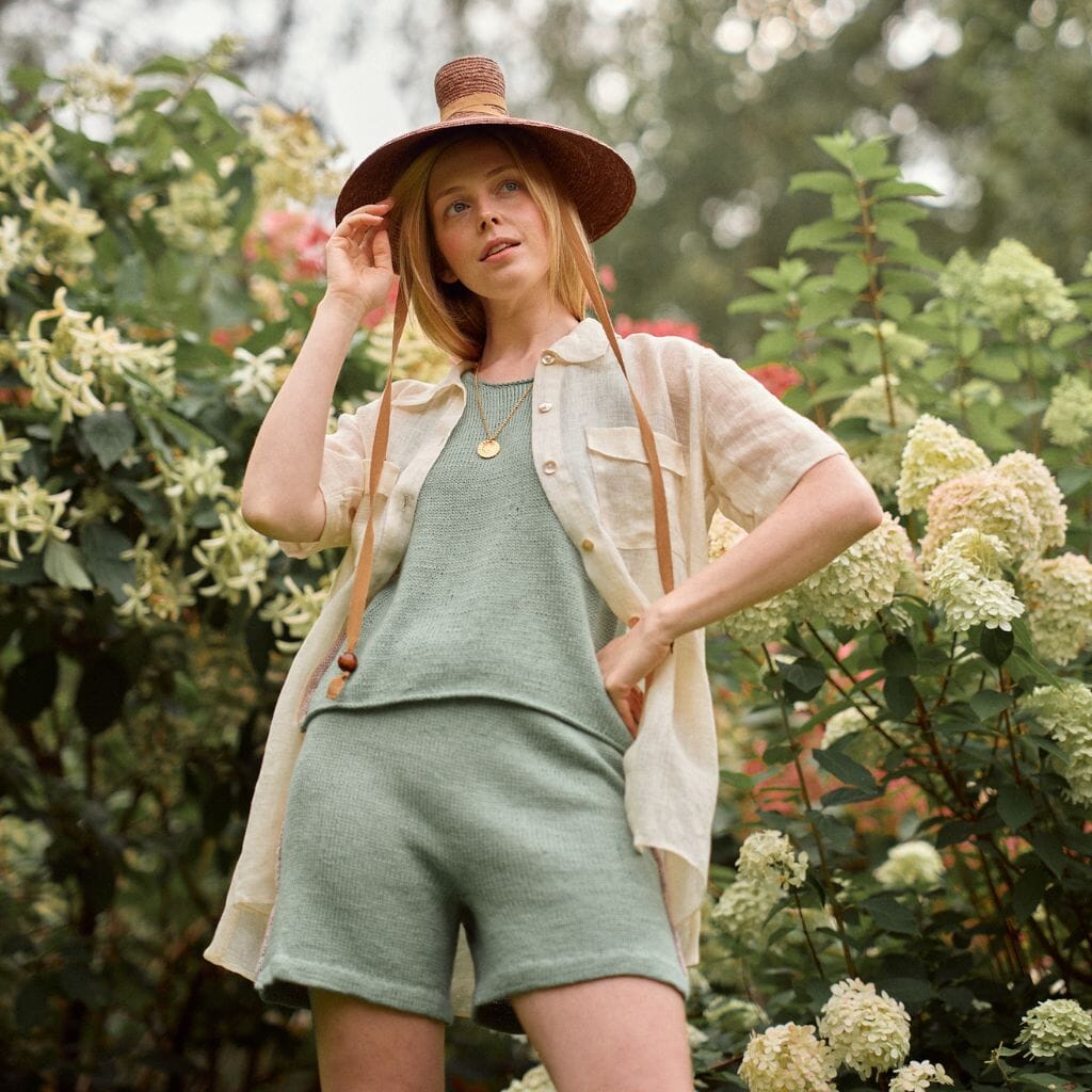 Woman in a green outfit and straw hat standing among flowers