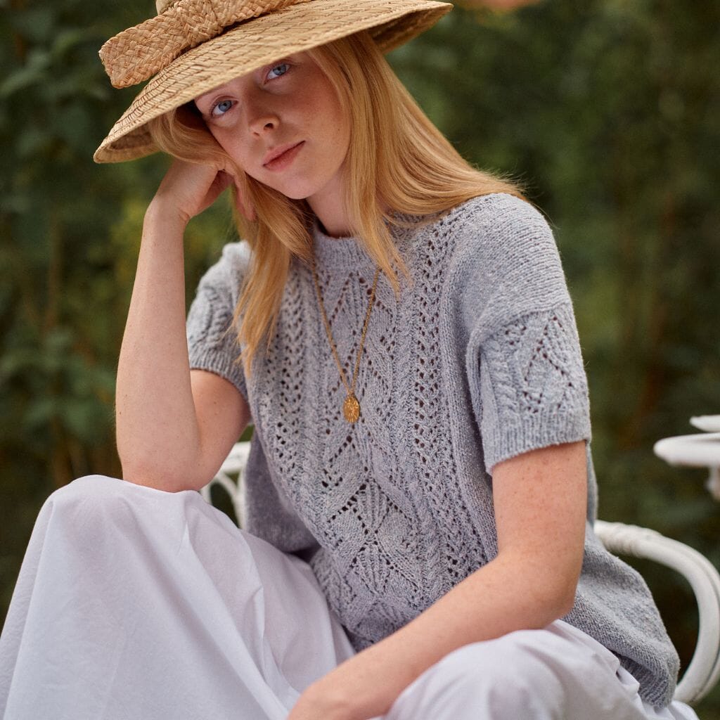 Woman wearing a straw hat and gray knit top sitting outdoors.