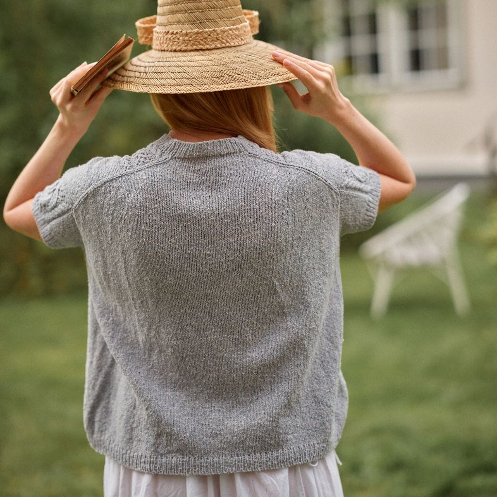 Person wearing a straw hat and gray cardigan in an outdoor setting