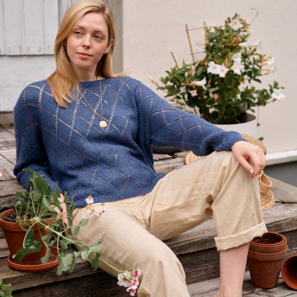 Woman wearing a blue sweater sitting on a wooden deck with plants around.