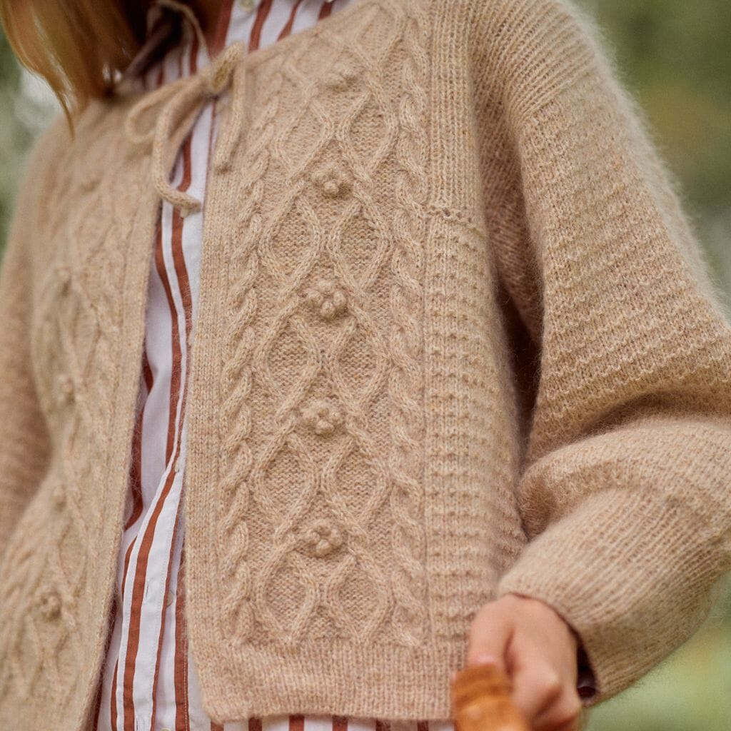 Close-up of a person wearing a beige knitted cardigan with a blurred background