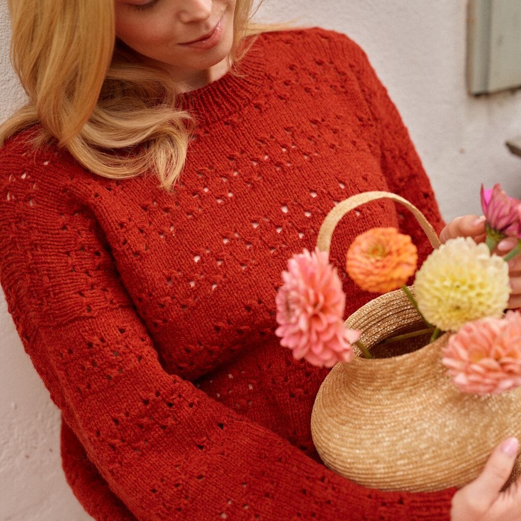 Woman in a red sweater holding a straw bag with flowers