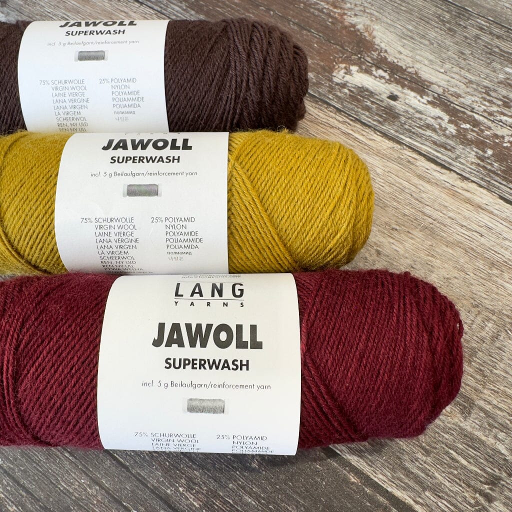 Three skeins of yarn in brown, yellow, and red with &#39;Jawoll Superwash&#39; labels on a wooden surface.
