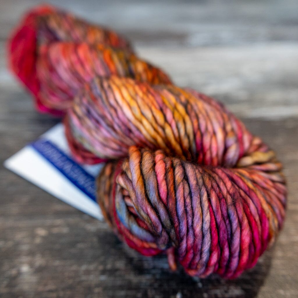 Multicoloured skein of yarn in pinks, reds and oranges on a wooden surface