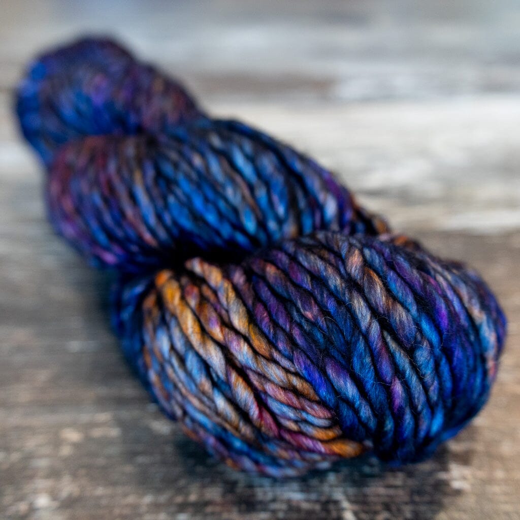 Multicoloured skein of yarn in blues, purples, and yellow on a wooden surface