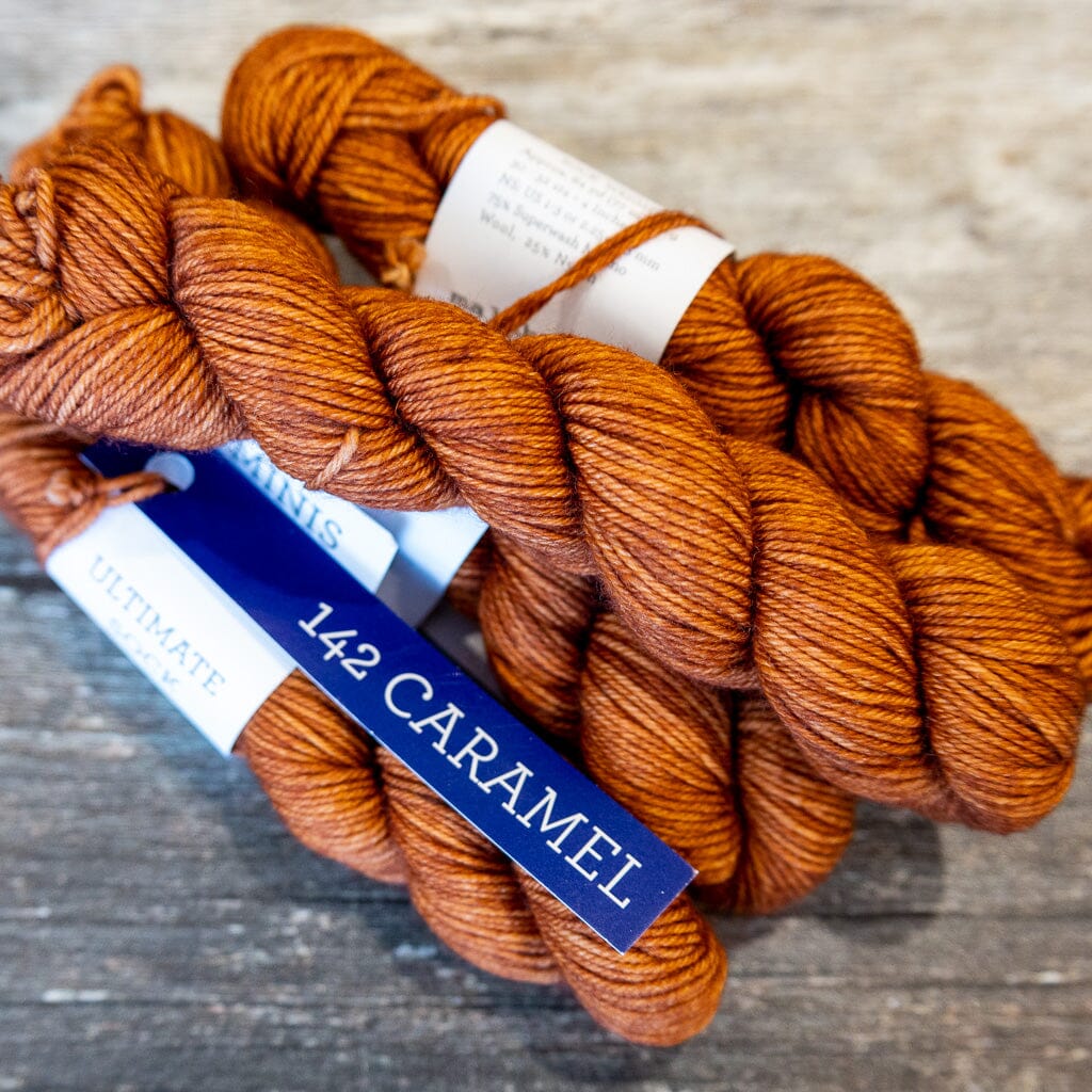 Balls of yarn labeled &#39;142 Caramel&#39; on a wooden surface