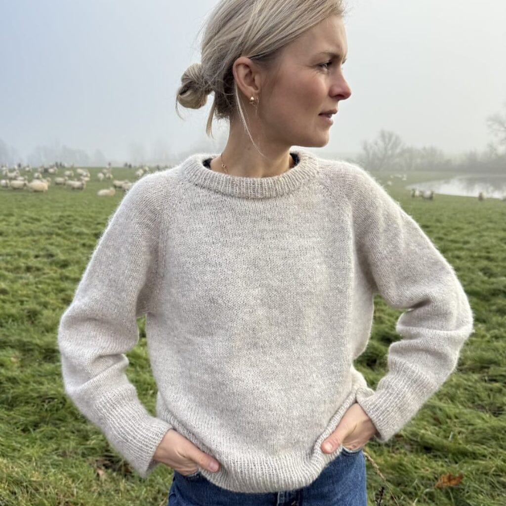 Woman wearing a light gray sweater in a field with sheep