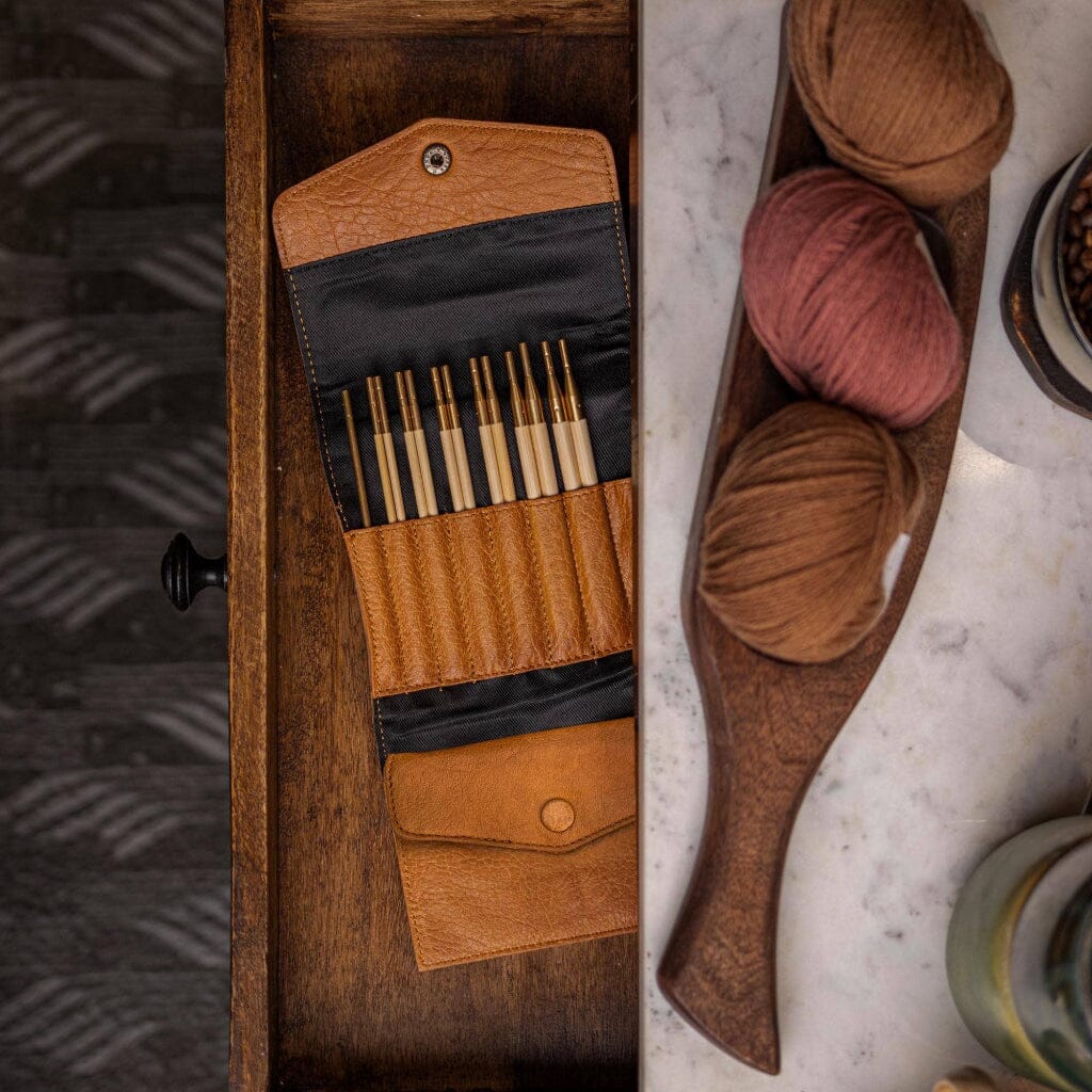 Wooden tray with needle case and yarn on a marble surface.