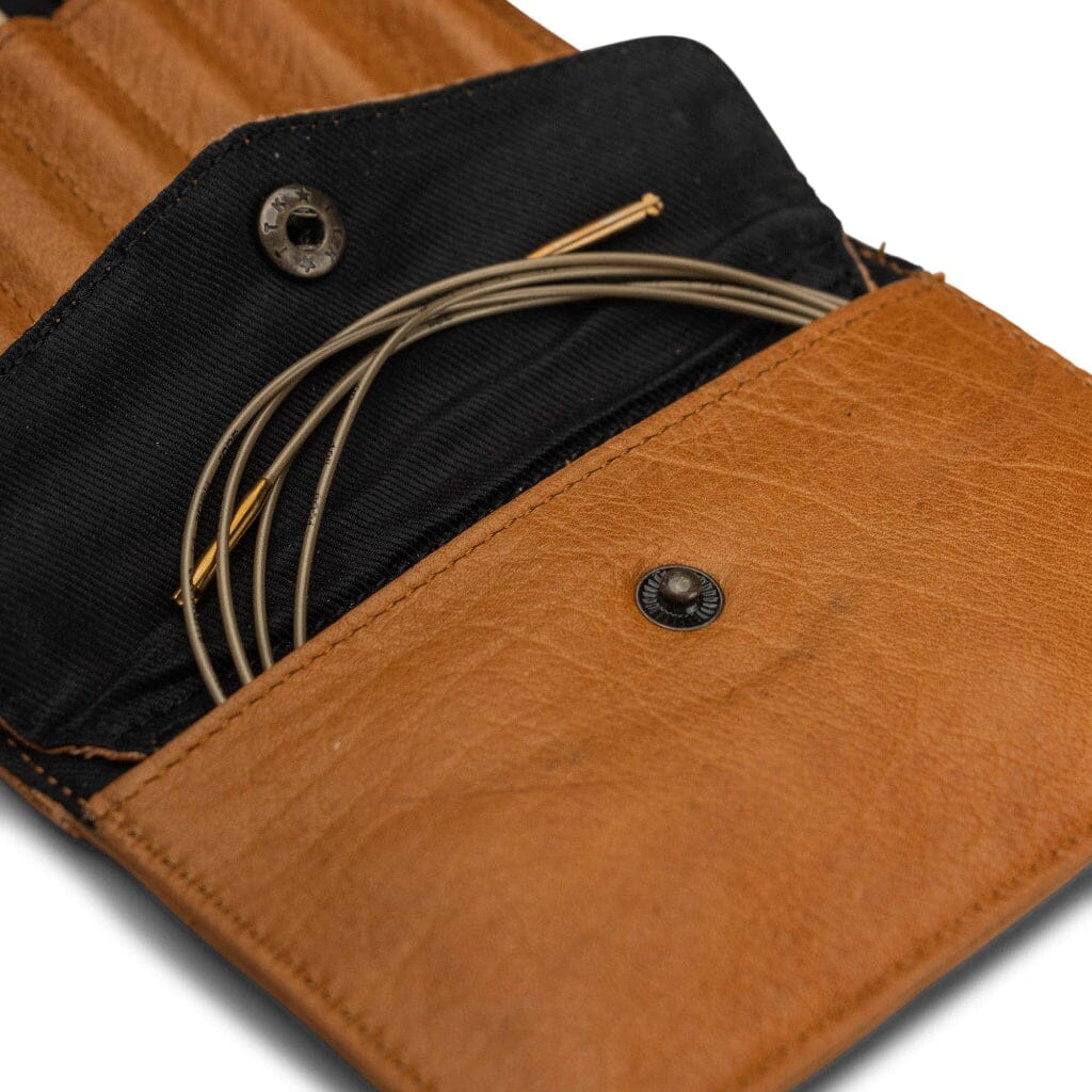 Brown leather case with black interior holding knitting needles on a white background