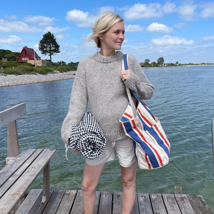 Woman standing on a wooden dock by a body of water, holding bags.