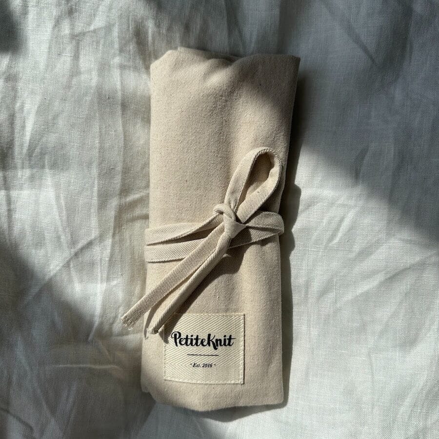 Rolled beige fabric with 'PetiteKnit' label on a textured surface