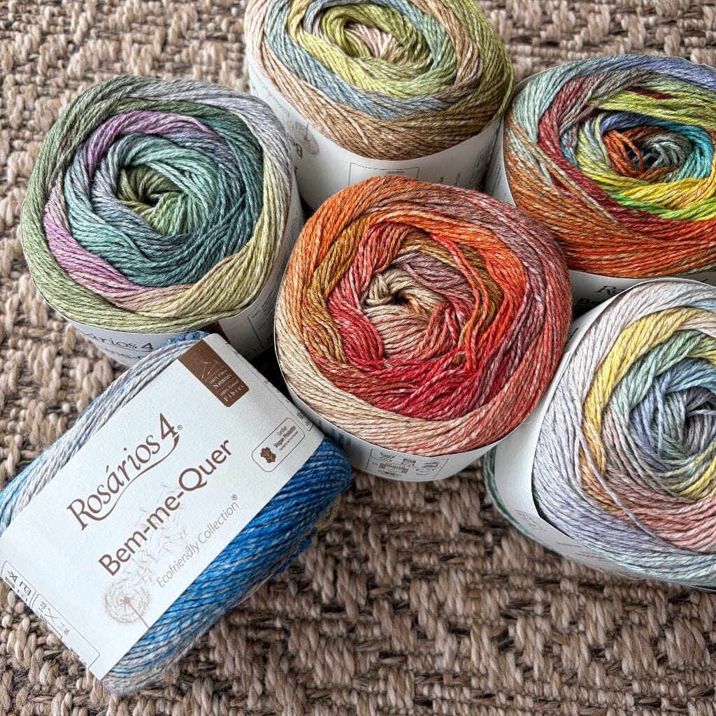 Five colorful yarn rolls on a textured surface with a label in front.