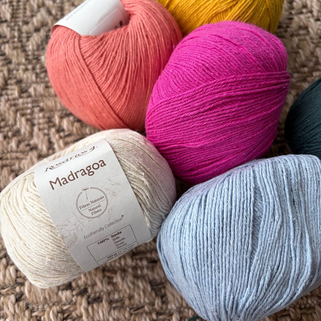 Five balls of silk yarn in different colors with a label on a textured surface