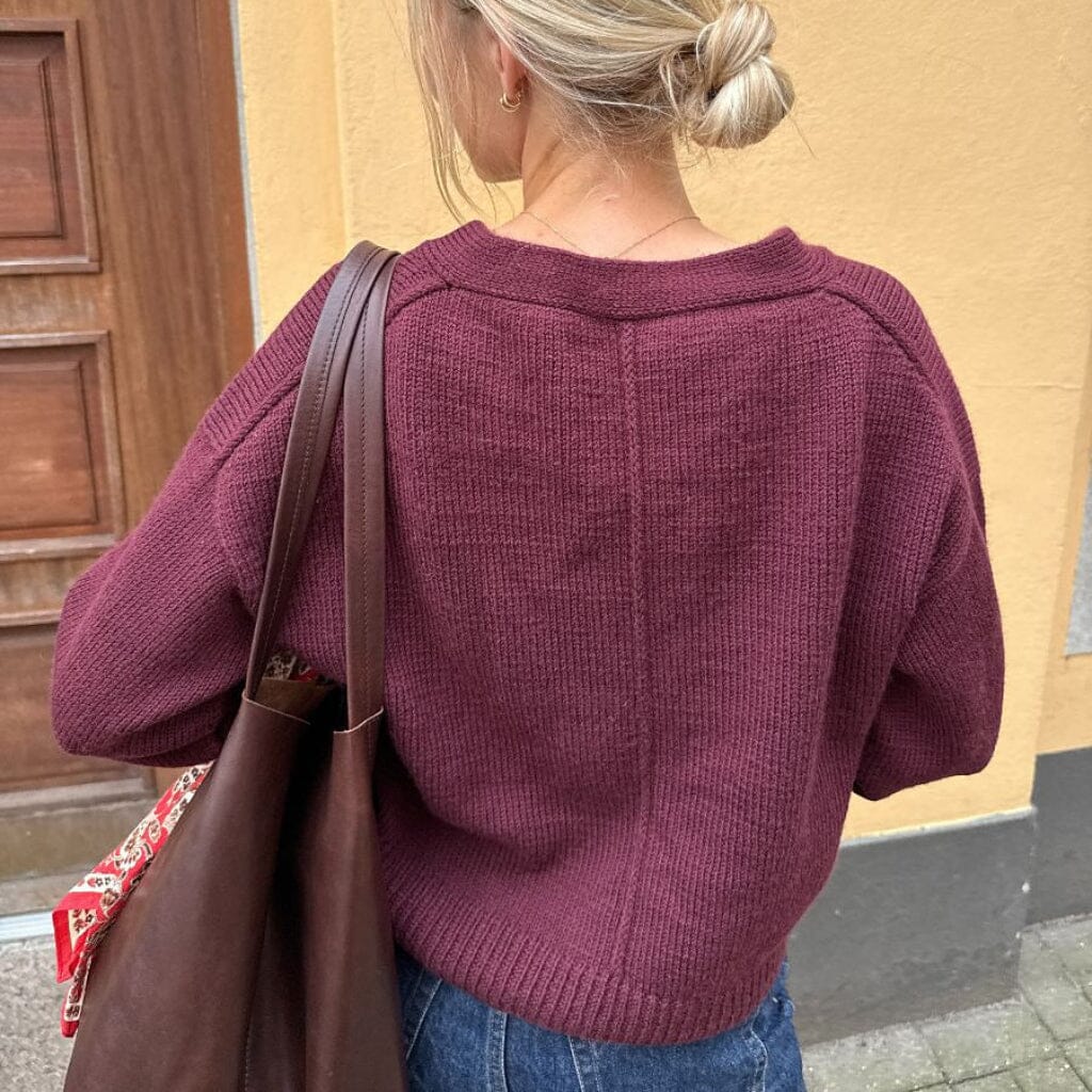 Person wearing a maroon sweater with a brown bag, standing against a beige wall.