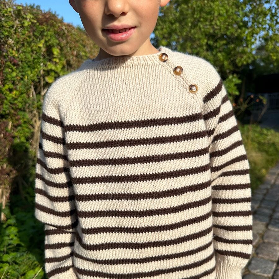 young boy wearing stripey knitted sweater stood in sun outsdie