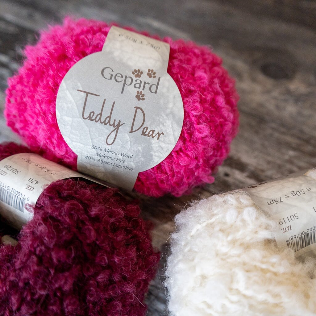 Three balls of yarn in pink, red, and white with &#39;Gepard Teddy Dear&#39; labels on a wooden surface.