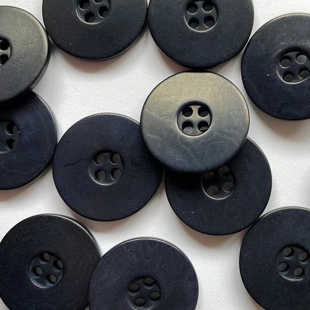 A pile of round navy buttons with four holes, photographed close-up on a white background.