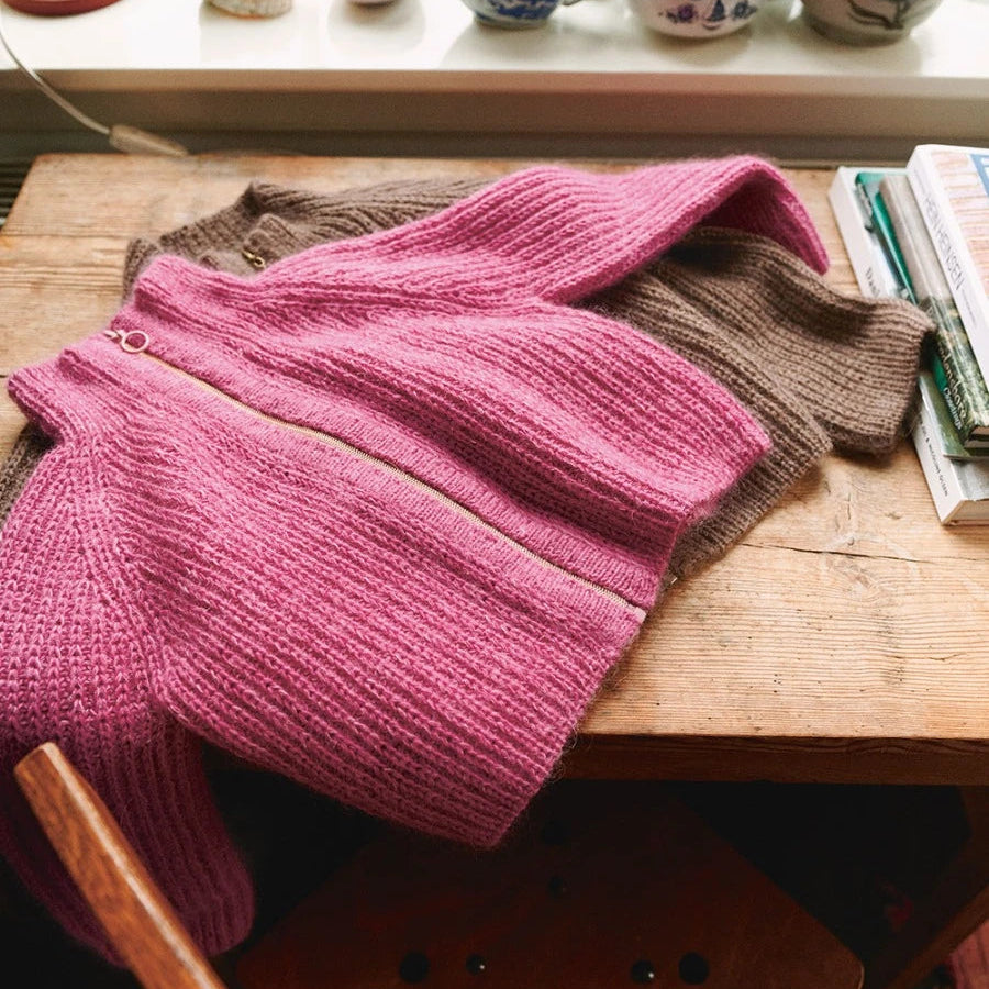 Pink and brown knitted items on a wooden surface with decorative vases in the background.