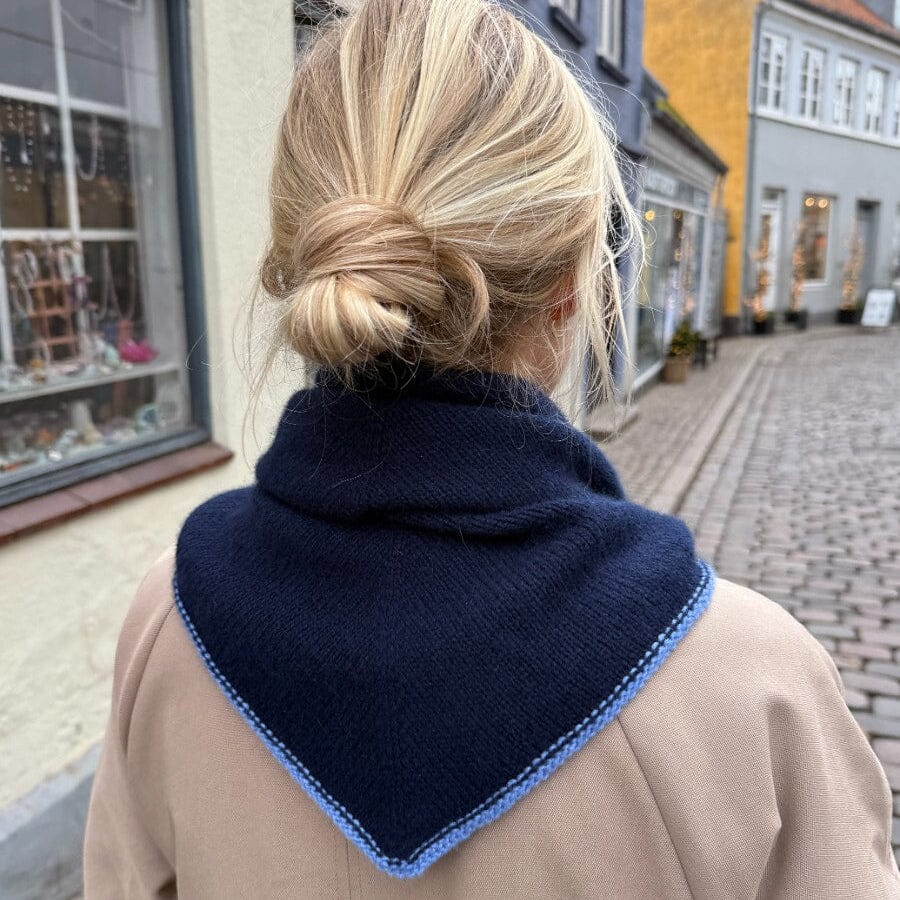 Person wearing a dark blue knitted scarf with a blue trim on a street.
