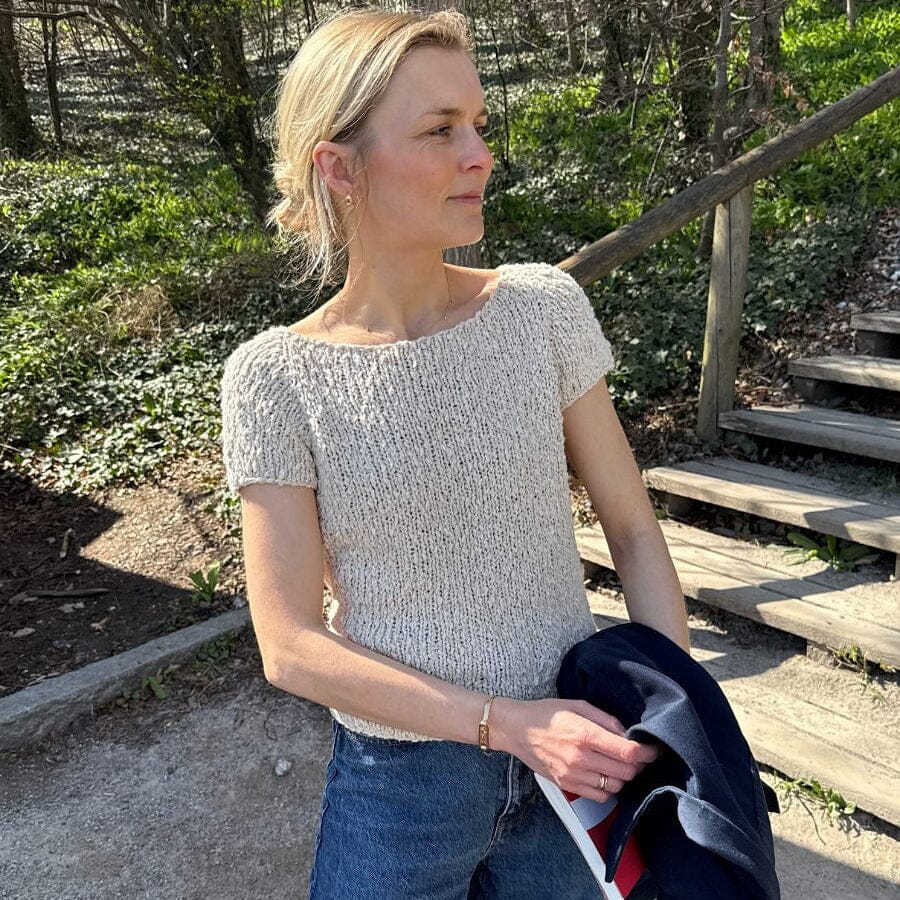 Woman in a textured white top and blue jeans holding a dark jacket outdoors.