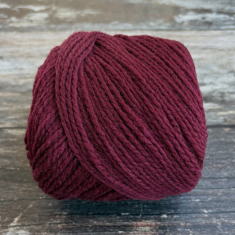 A ball of deep burgundy yarn resting on a rustic, weathered wooden surface.