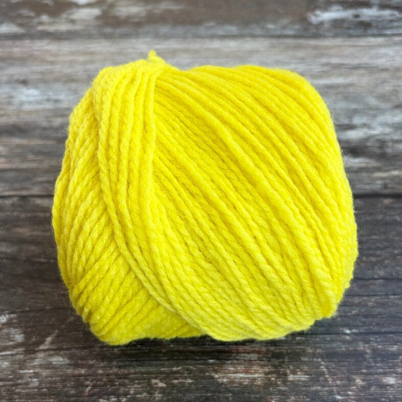 A bright yellow ball of yarn resting on a rustic, weathered dark wood surface.